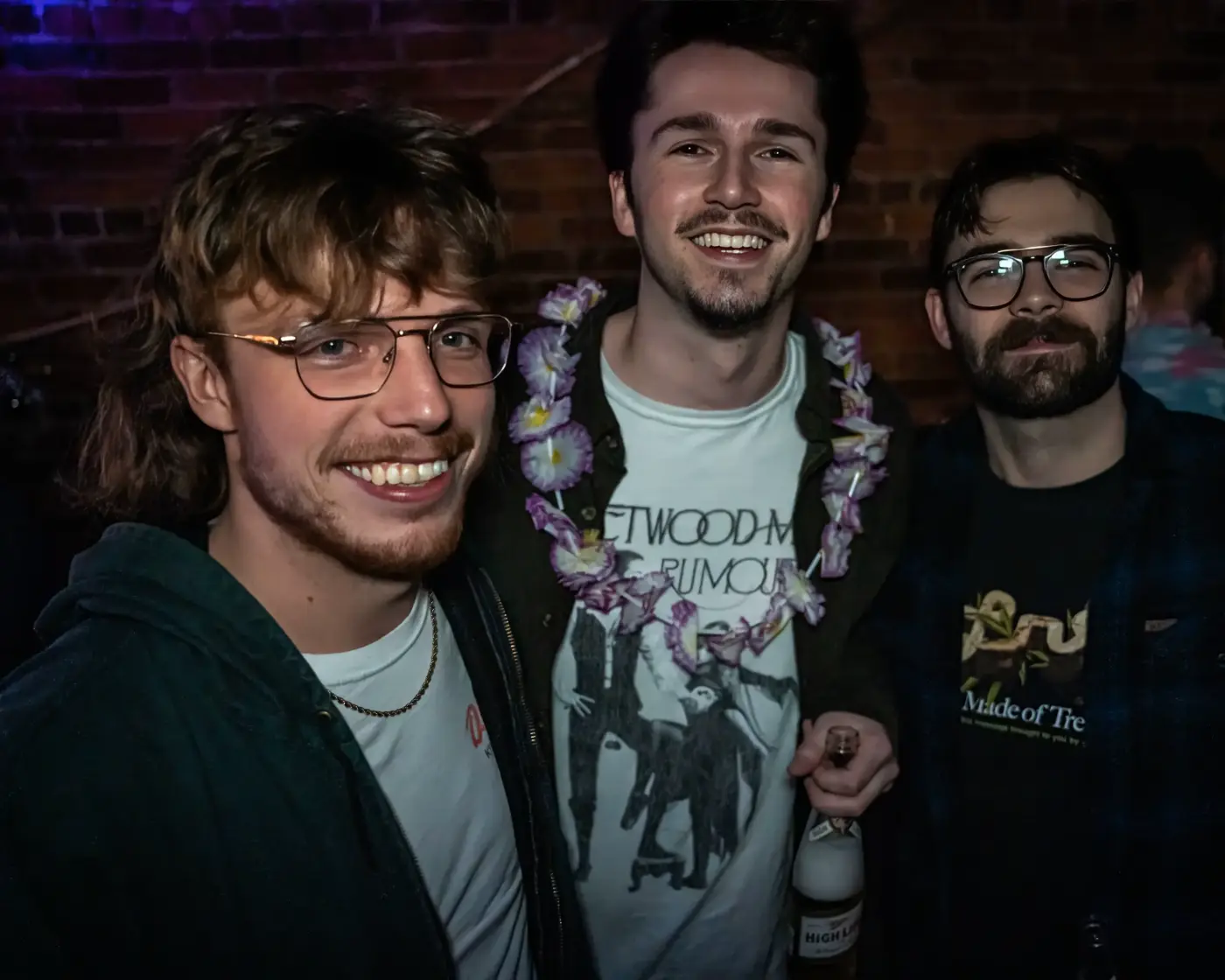 Three attendees posing together in front of a brick wall at a Pluto Events party
