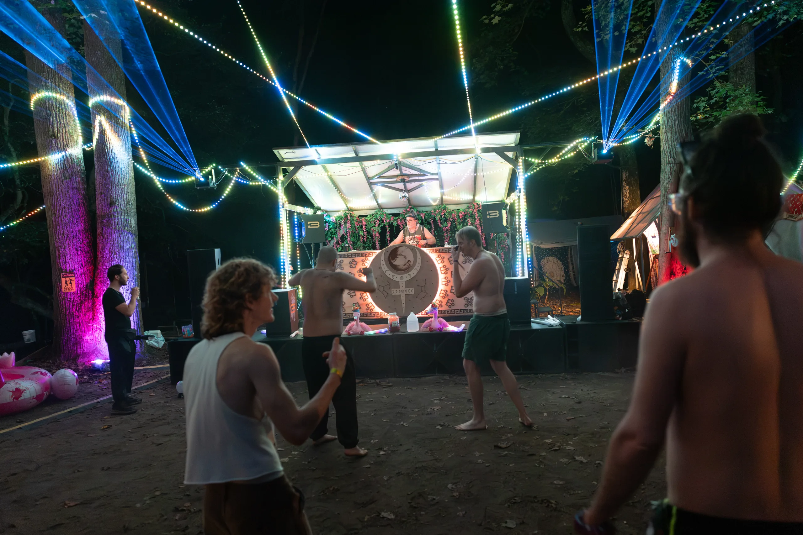 Attendees dancing in front of a forest stage beneath string lights at ManaFest 2026