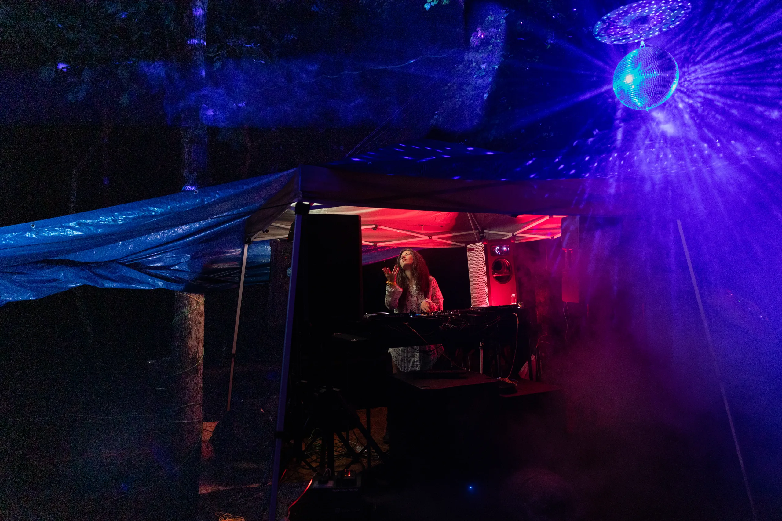 A DJ performing beneath a disco ball and blue light beams at ManaFest 2026