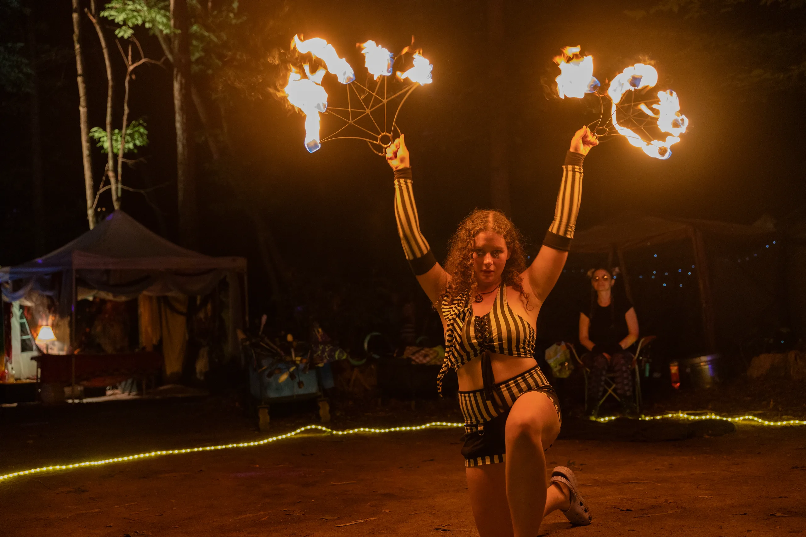 A fire performer holding flaming fans overhead at ManaFest 2026