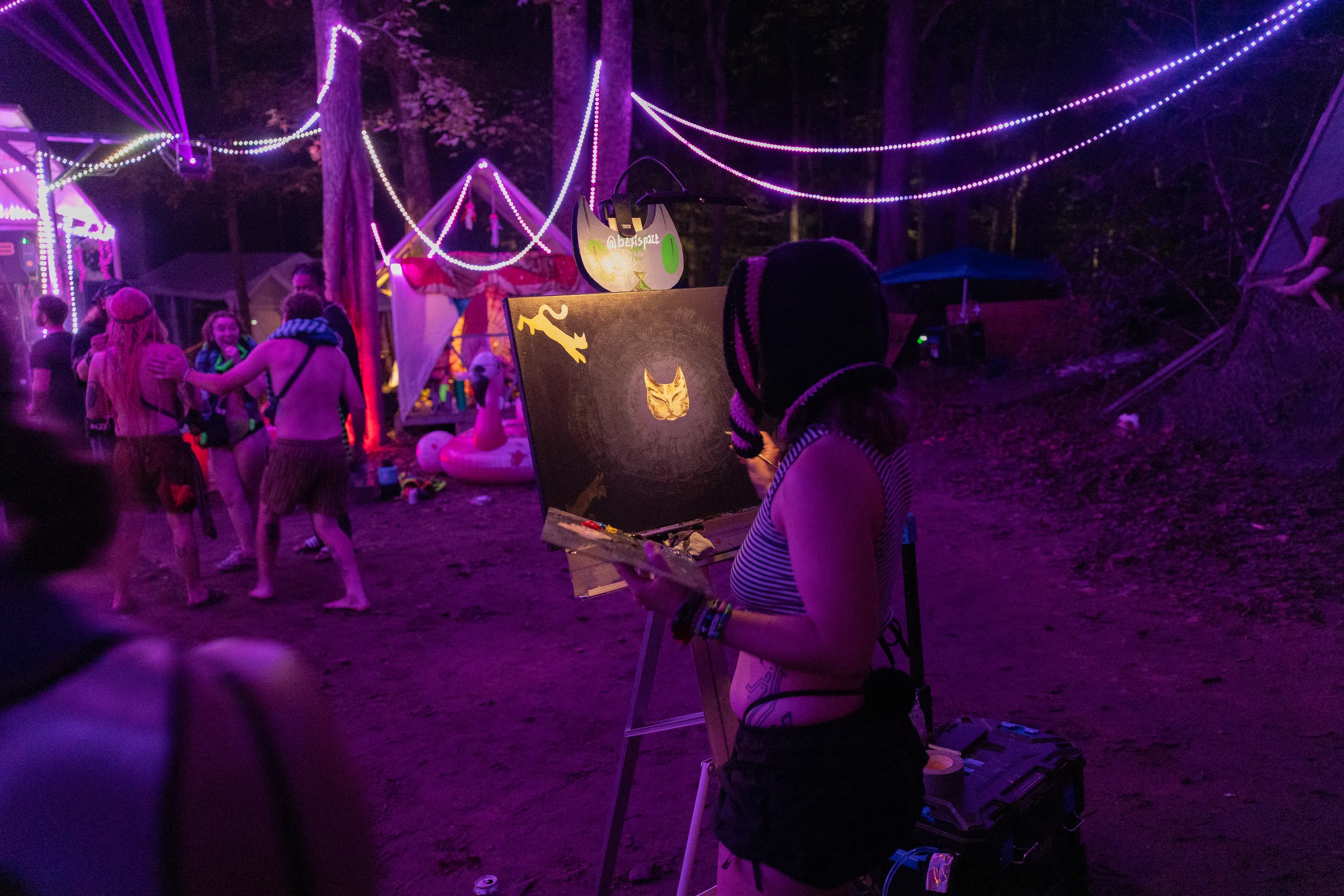 An artist painting beside the dance floor under purple lights at ManaFest 2026
